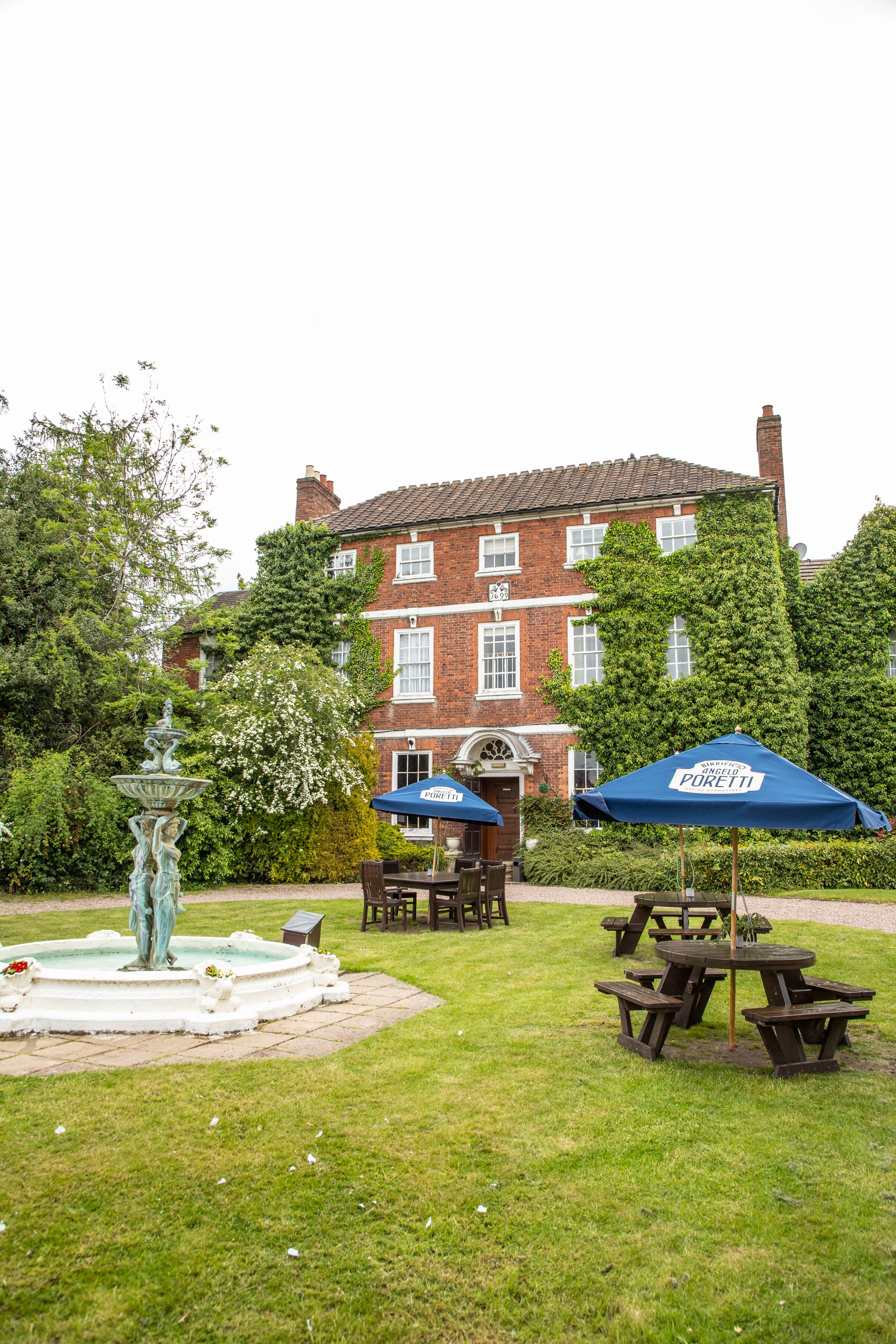 A garden with a fountain, picnic tables, and a building with a red brick facade.