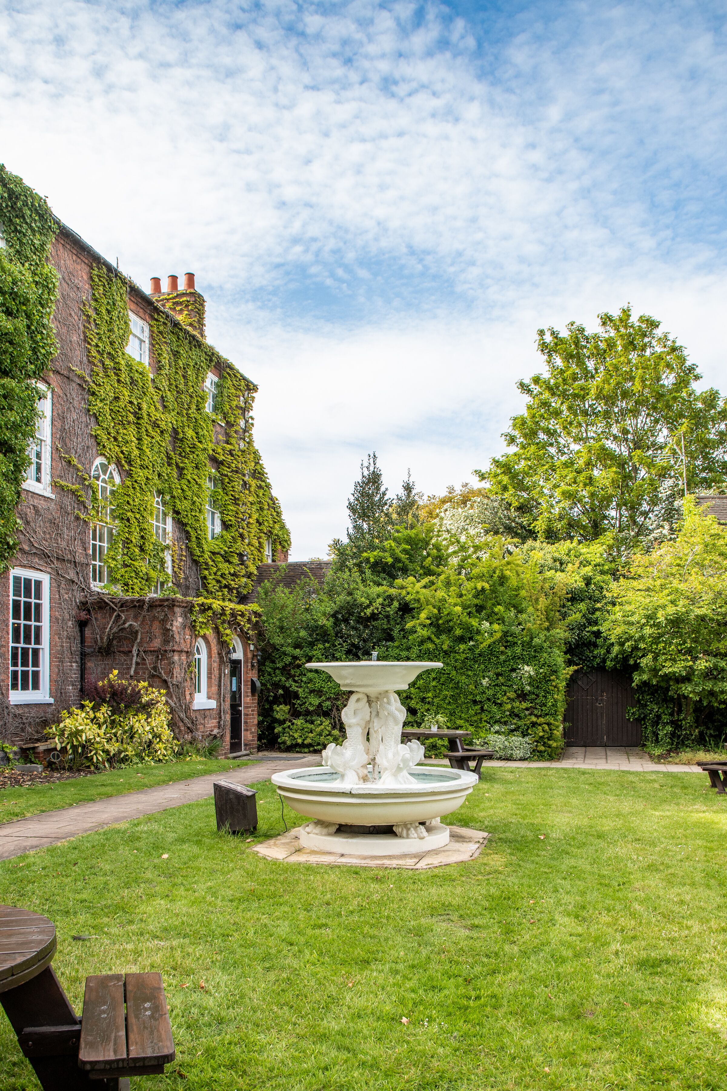 A courtyard with a fountain, a picnic table, and a building with ivy-covered walls.