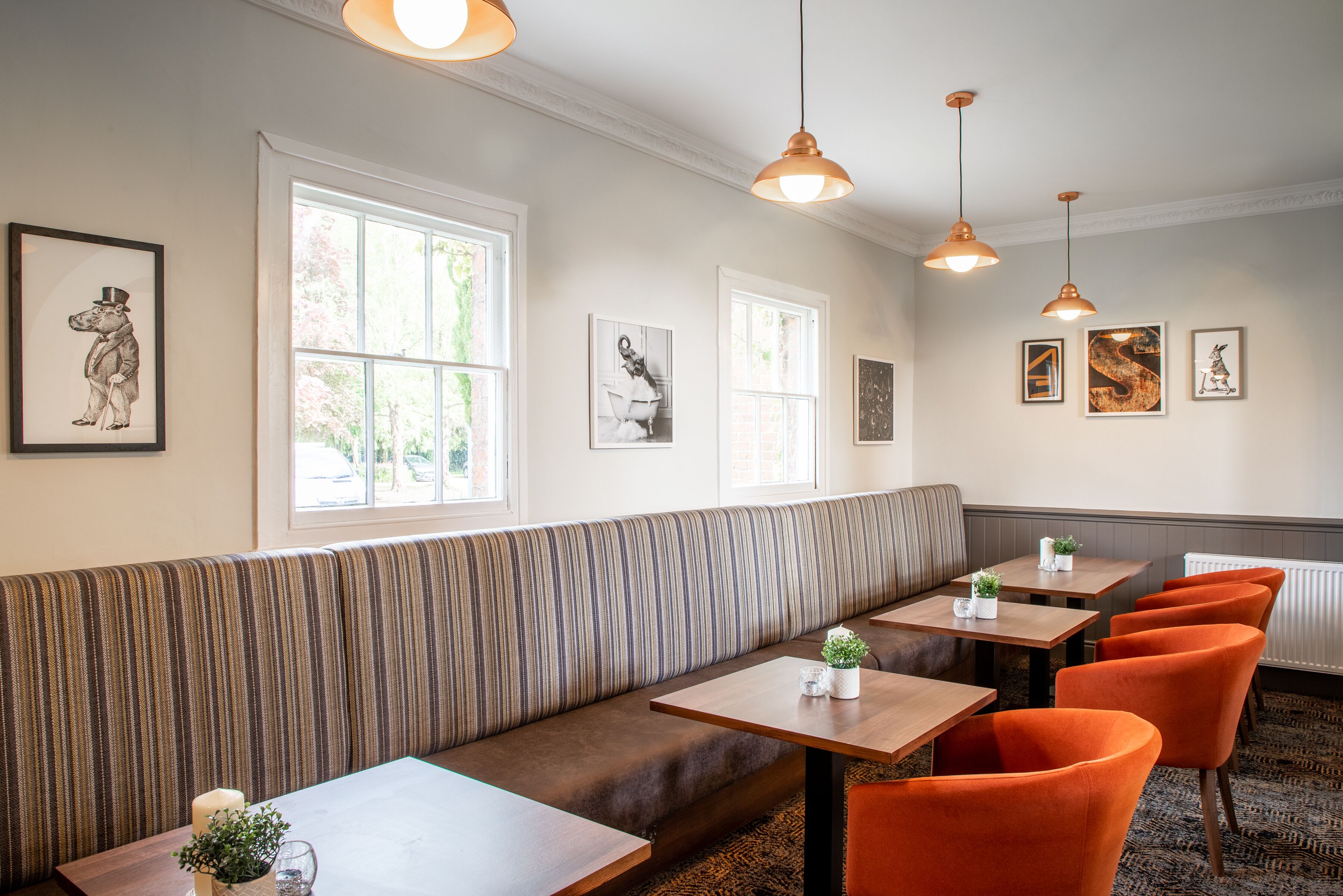 Un restaurant avec un banc à rayures, des tables, des chaises orange, des luminaires suspendus et des œuvres d’art encadrées accrochées aux murs.