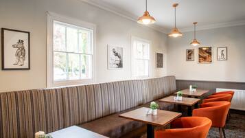 Un restaurant avec un banc à rayures, des tables, des chaises orange, des luminaires suspendus et des œuvres d’art encadrées accrochées aux murs.