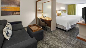 A hotel room with a sofa, a desk with a phone, a bed, and a TV.