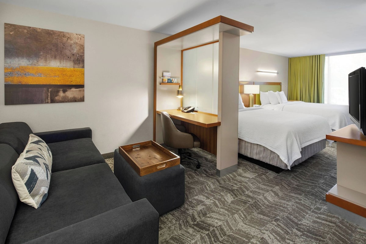 A hotel room with a sofa, a desk with a phone, a bed, and a TV.