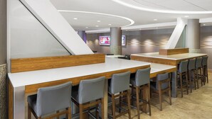 A modern bar area with wooden tables and grey chairs, a large screen, and a unique ceiling design.