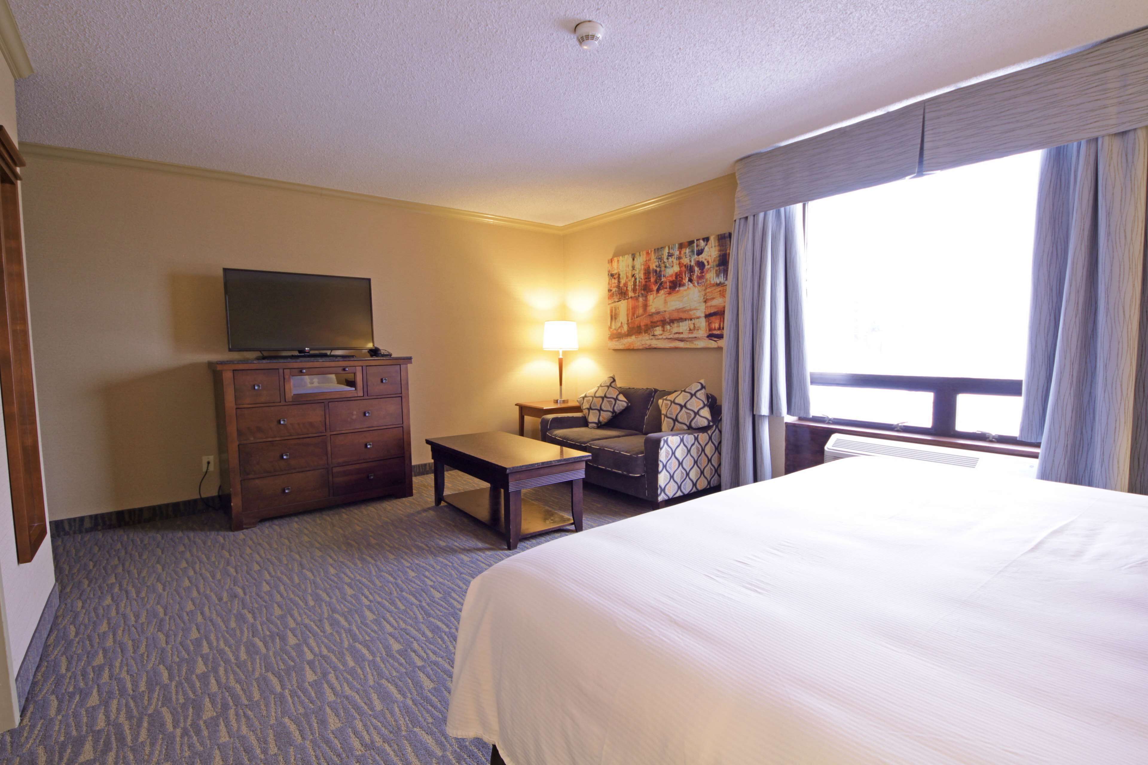 A hotel room with a large bed, a television on a dresser, a small table, a couch, and a window with curtains.