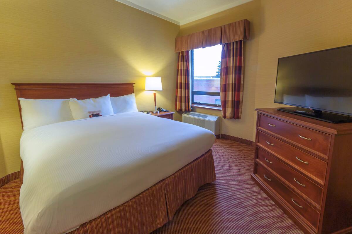 A hotel room with a large bed, a TV on a wooden dresser, and a window with curtains.