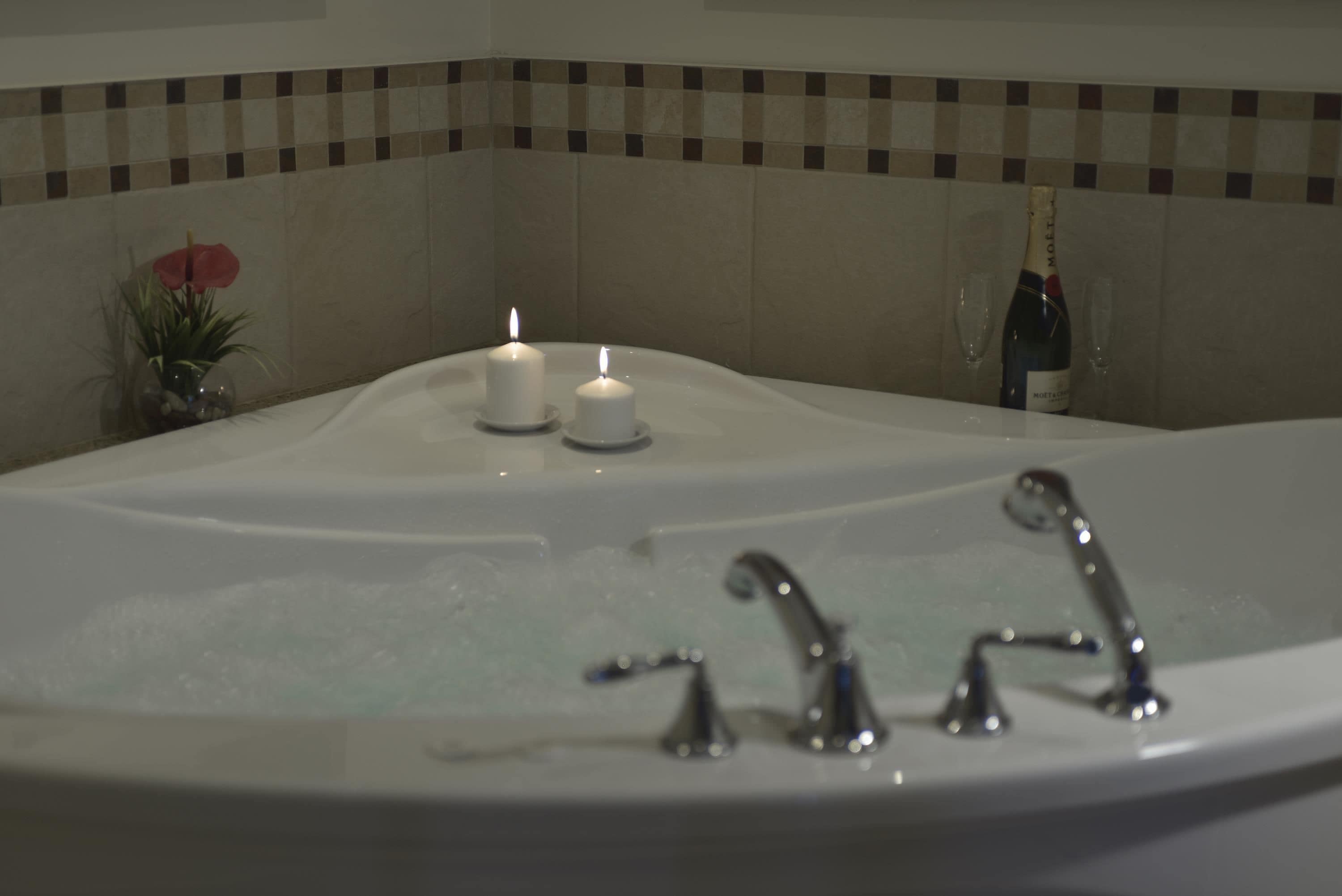 A bathtub with two lit candles and a bottle of champagne.