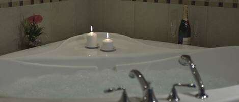 A bathtub with two lit candles and a bottle of champagne.