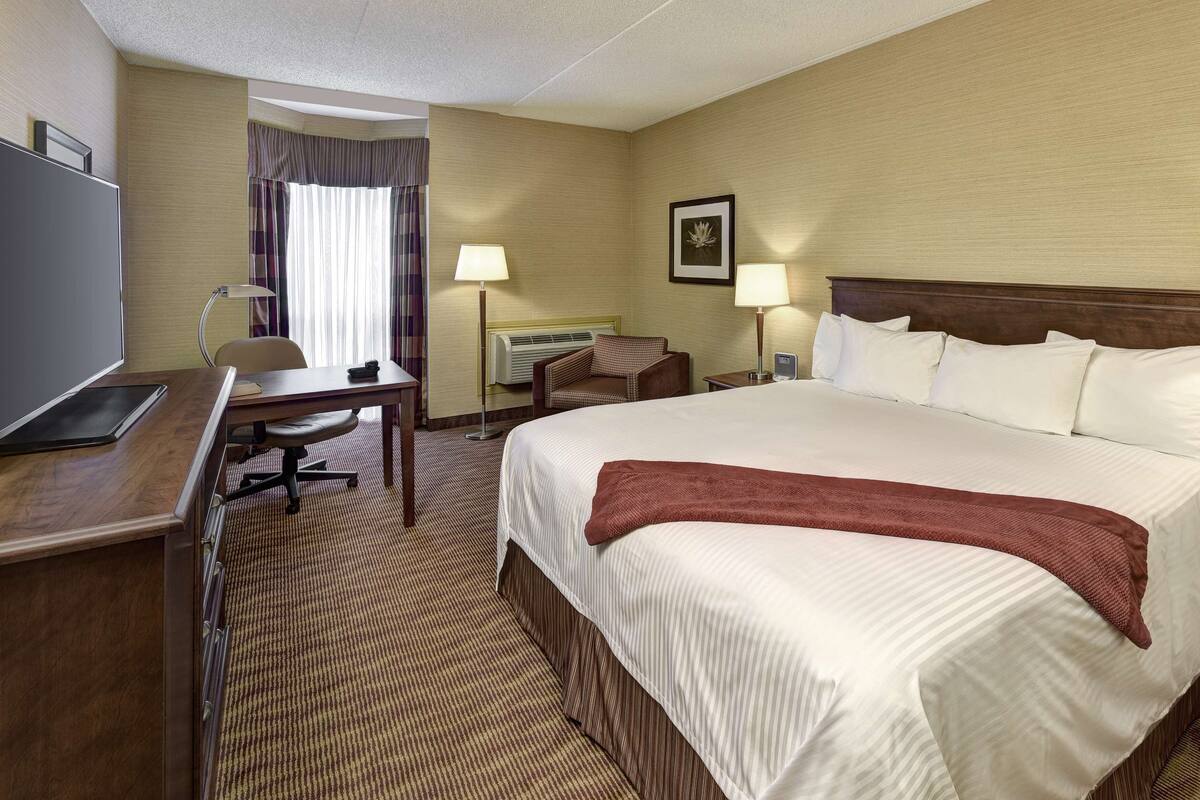 Une chambre d’hôtel avec un grand lit, un bureau avec une chaise, une télévision et une fenêtre avec des rideaux.