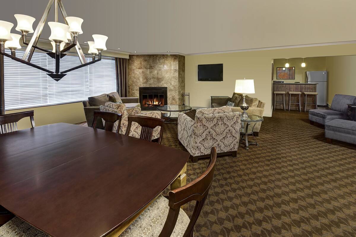 A spacious living room with a fireplace, a dining area with a large table and chairs, and a separate seating area with sofas and a TV.