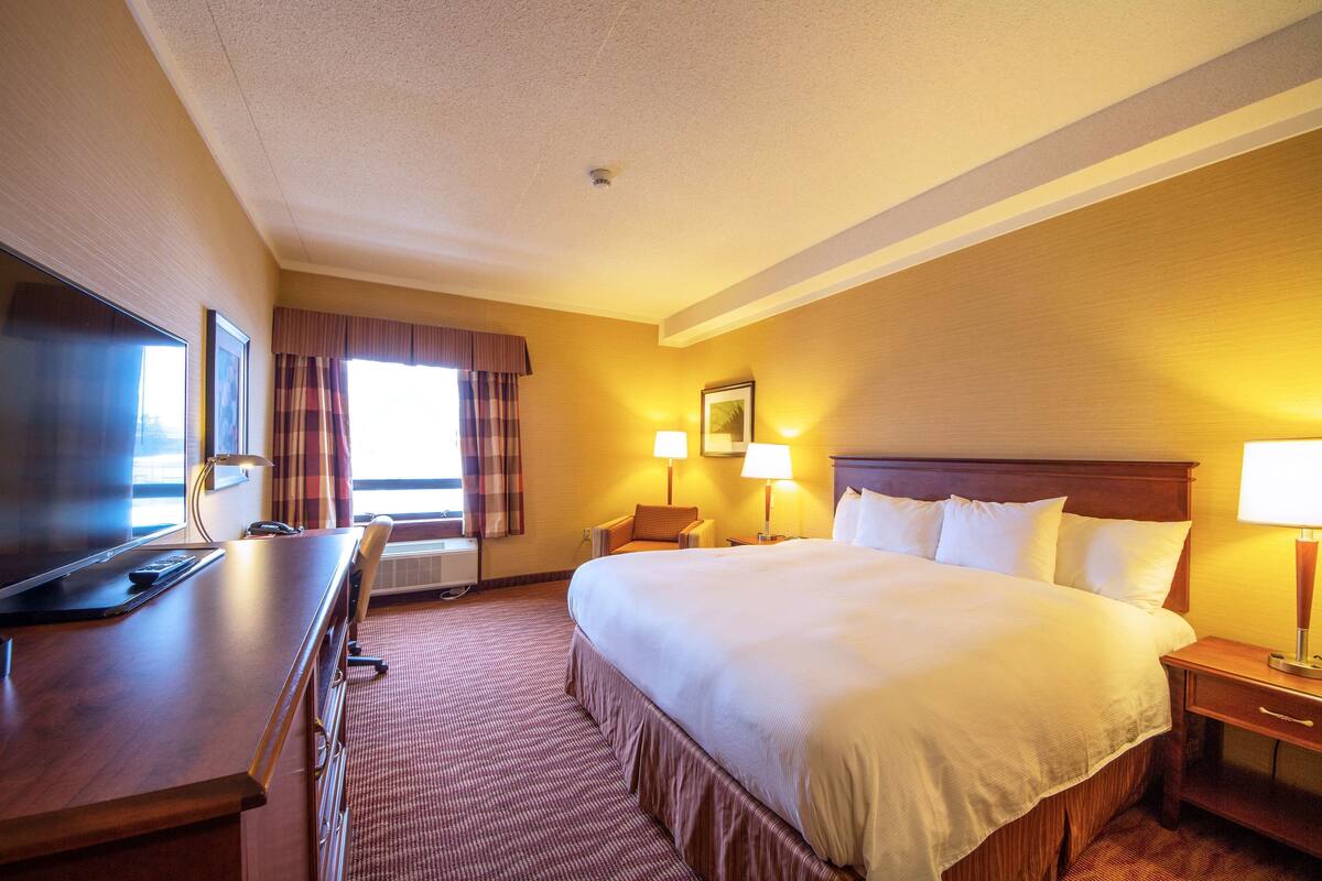Une chambre d’hôtel avec un grand lit, un bureau, une chaise, deux lampes de chevet et un téléviseur.