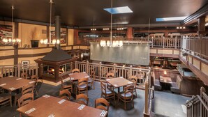 Restaurante com várias áreas de refeição, incluindo uma lareira central e um mezanino com mais lugares.