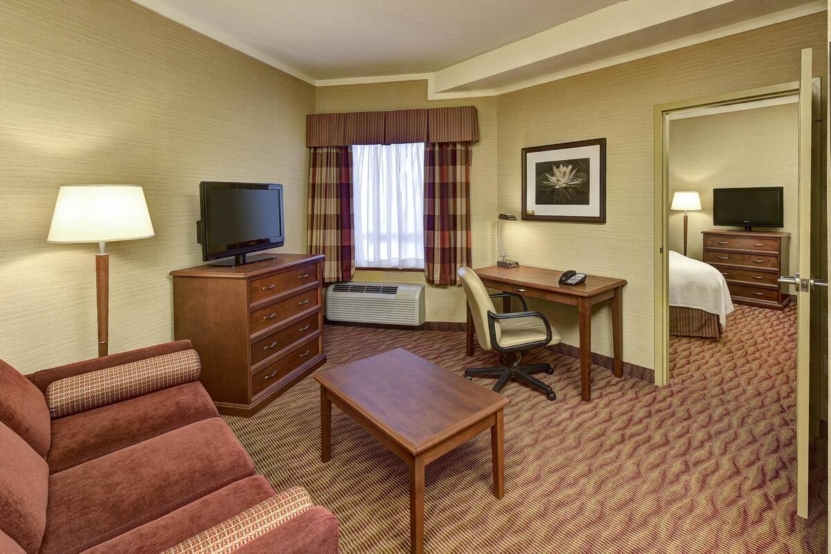 A hotel room with a sofa, a desk, a chair, a TV, a dresser, and a framed picture on the wall.