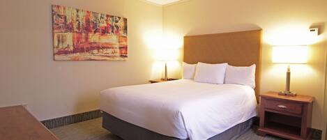 A hotel room with a large bed, two bedside tables with lamps, a wooden nightstand, and a colorful abstract painting on the wall.