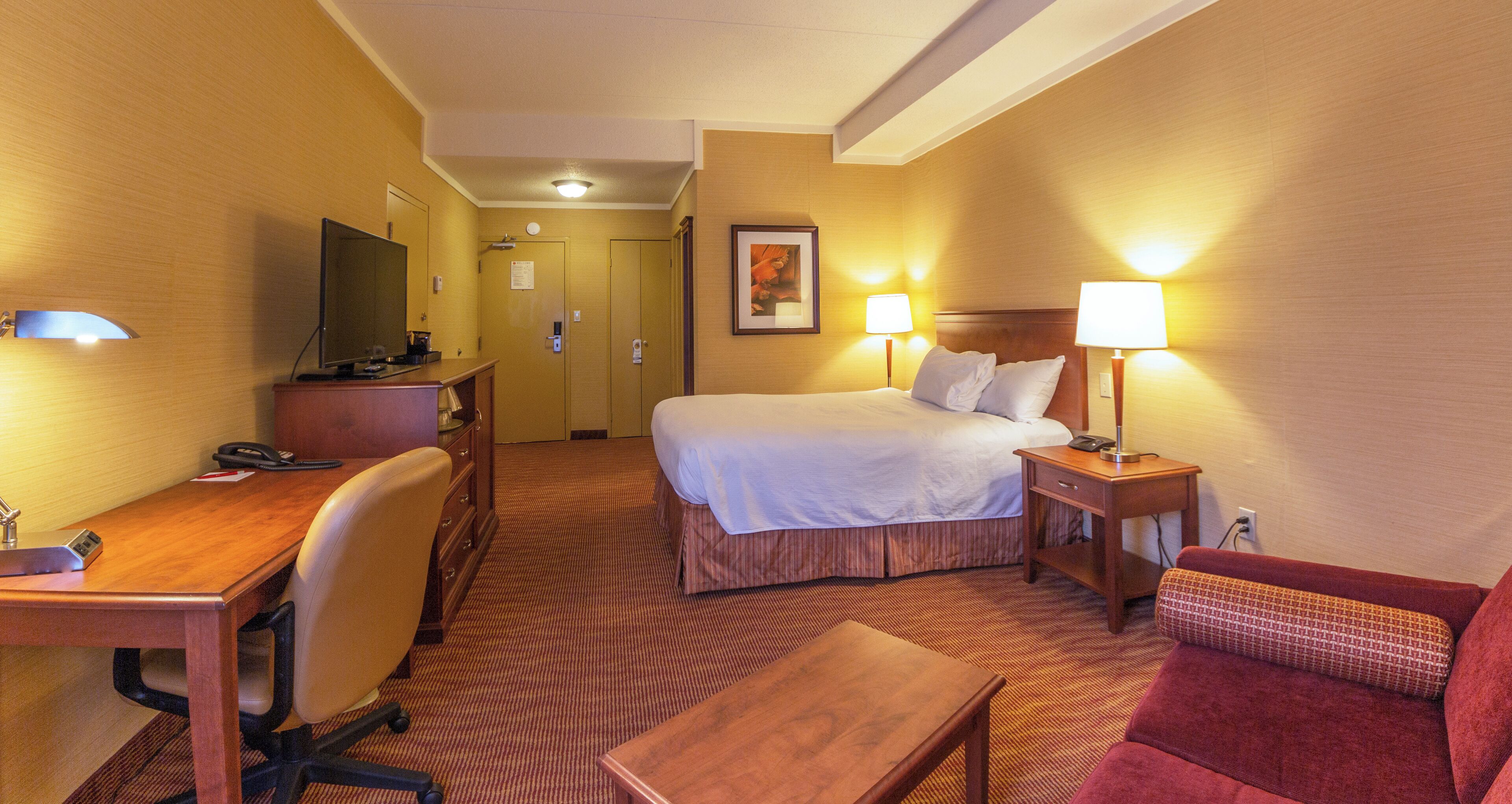 A hotel room with a bed, desk, chair, and a TV.