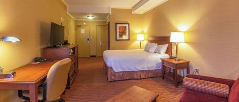 A hotel room with a bed, desk, chair, and a TV.