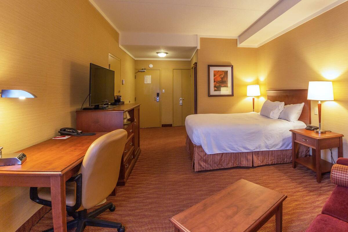 A hotel room with a bed, desk, chair, and a television.