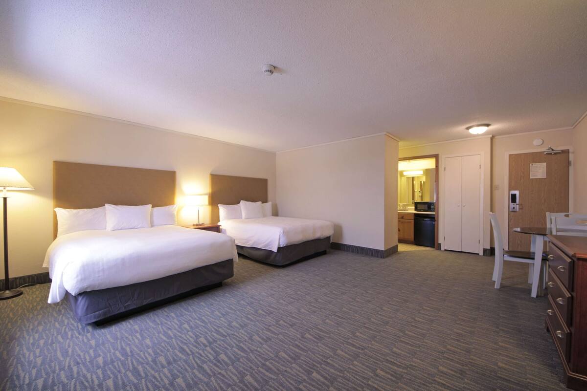 A hotel room with two beds, a desk, a chair, and a kitchenette.