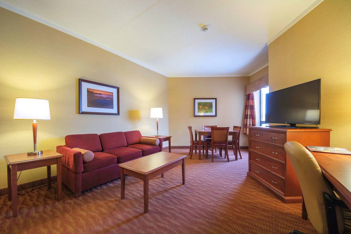 A hotel room with a red sofa, a wooden coffee table, a TV on a wooden cabinet, and two lamps.