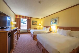 Habitación de hotel con dos camas, un escritorio, un televisor y una ventana con cortinas.