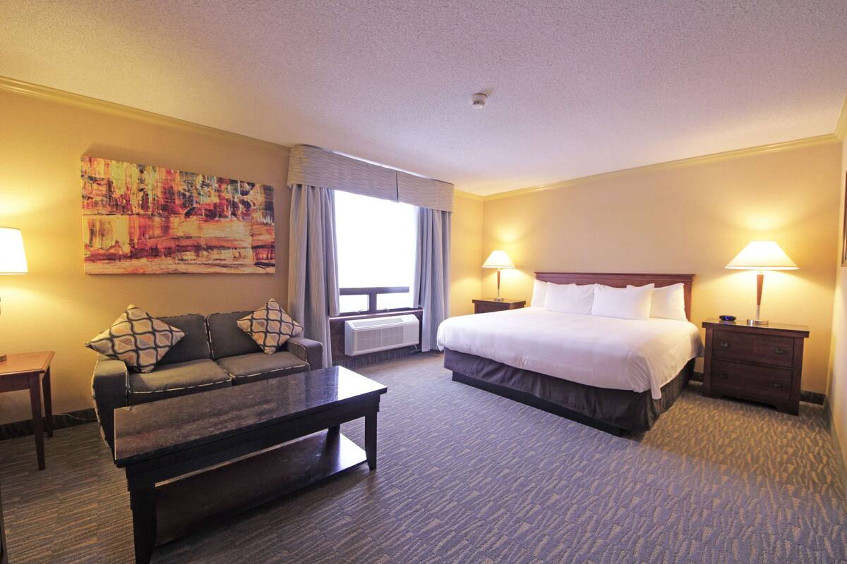 A hotel room with a bed, a sofa, a coffee table, and two lamps.