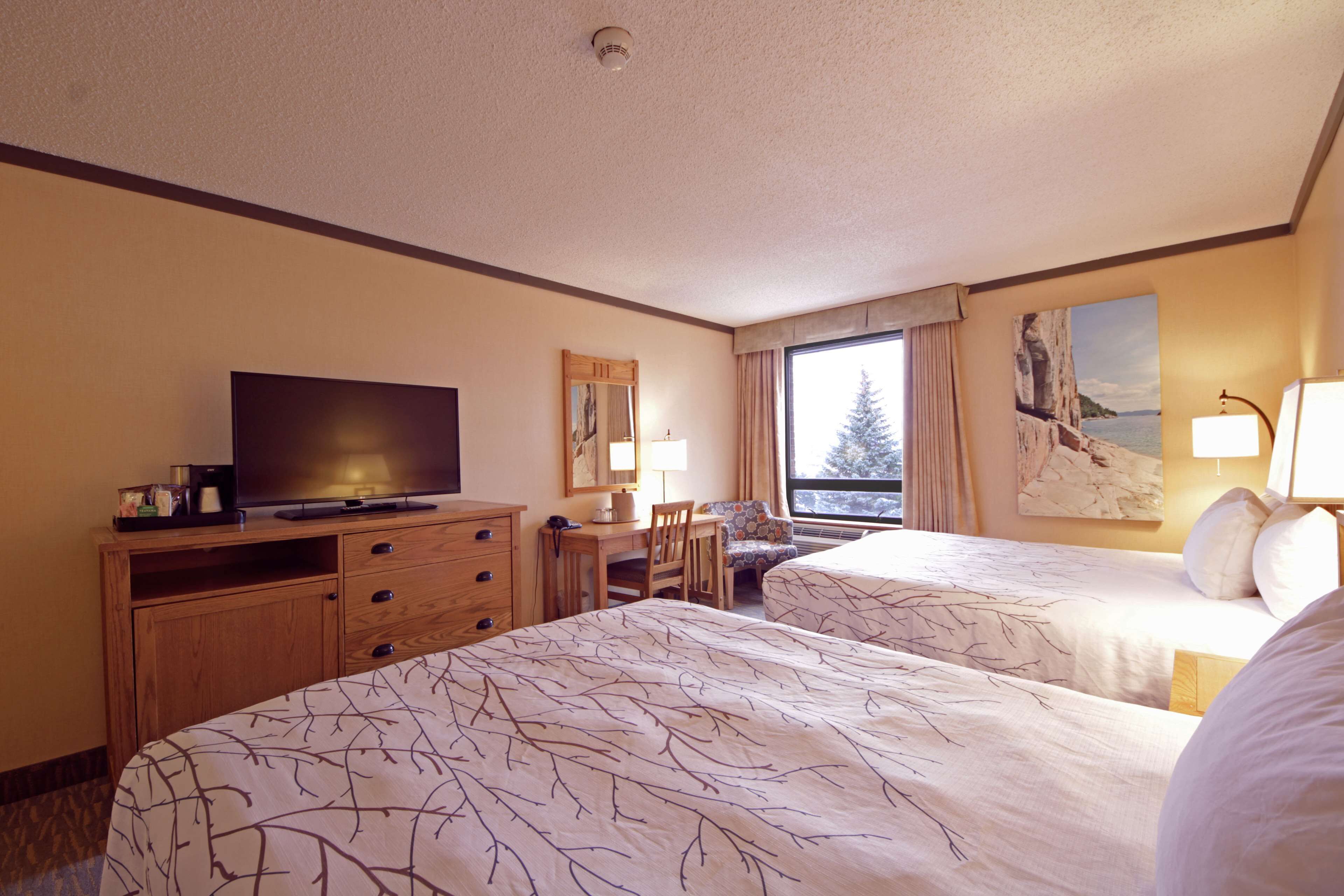 A hotel room with two beds, a TV, a desk, and a window with a view.