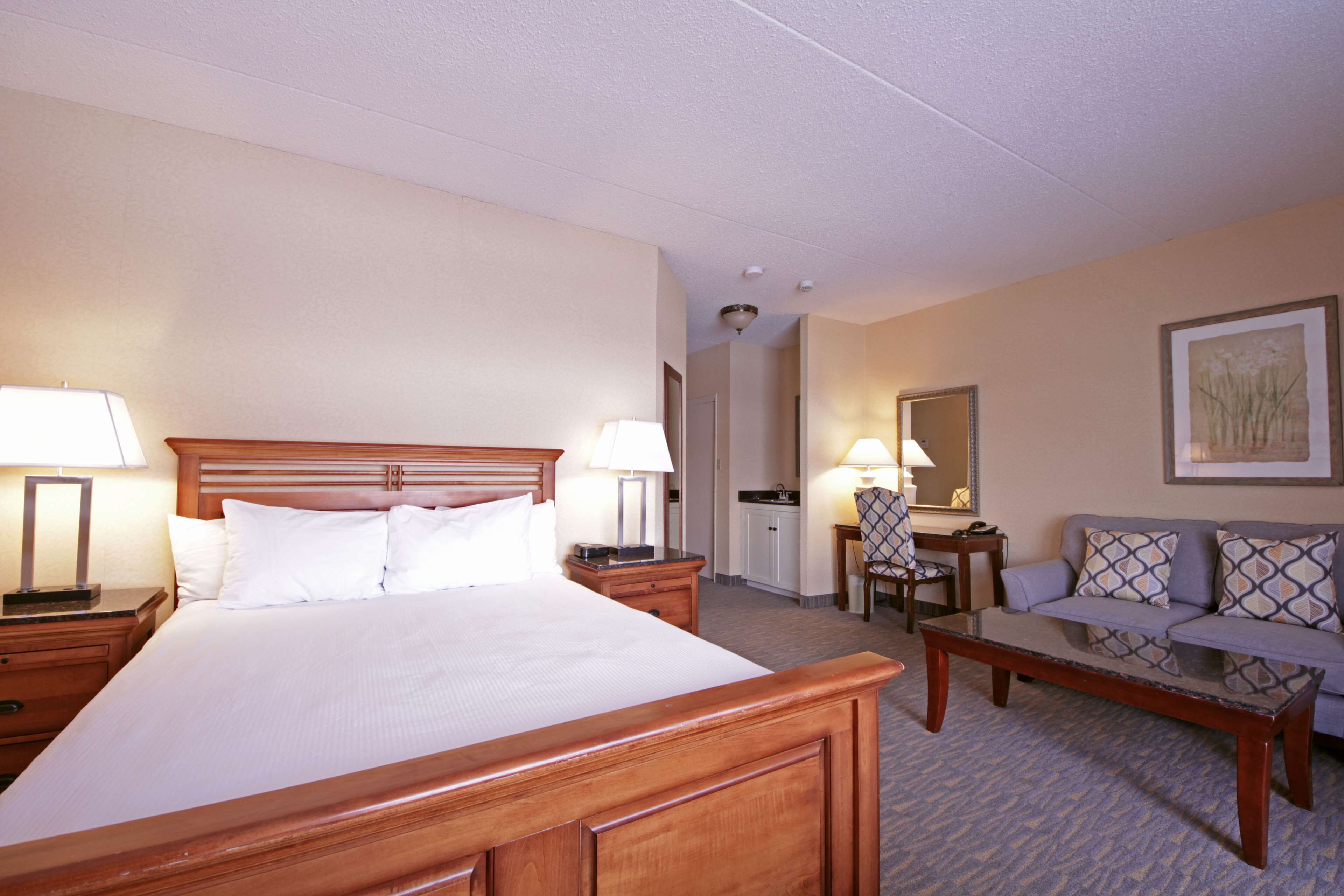 Une chambre d’hôtel dotée d’un grand lit, d’une tête de lit en bois, d’un coin salon avec un canapé et une table, ainsi que d’un petit bureau avec une chaise.