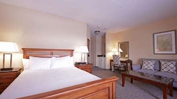 A hotel room with a large bed, a wooden headboard, a seating area with a sofa and a table, and a small desk with a chair.