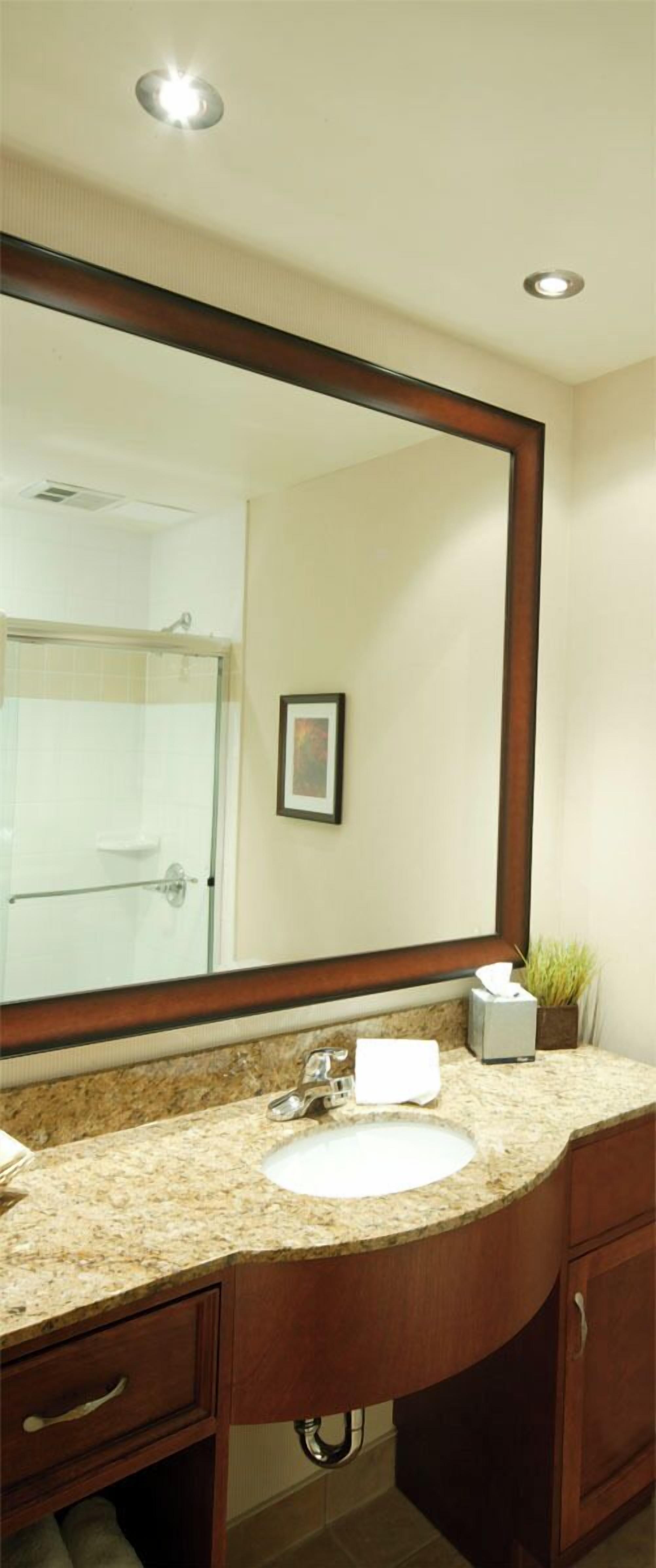 A bathroom with a large mirror, a sink, a towel dispenser, and a potted plant.