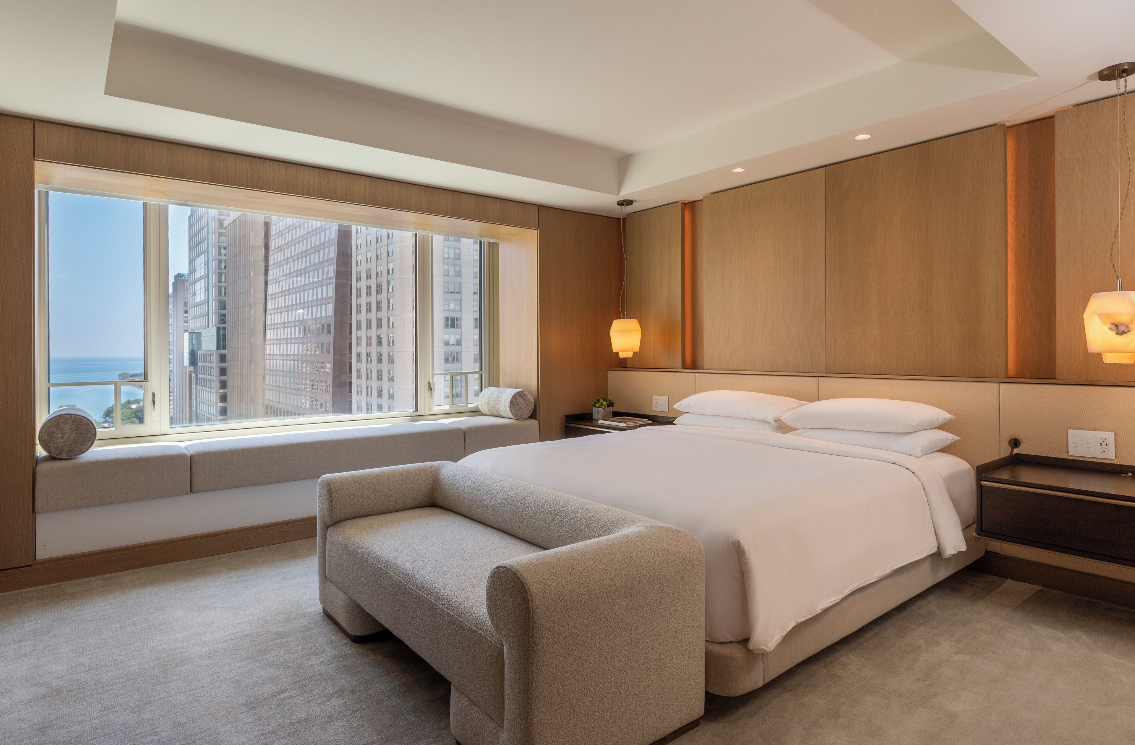 Una habitación de hotel moderna con una cama grande, una zona de estar, una mesita de noche y vistas a edificios altos.
