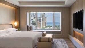 Quarto de hotel moderno com uma cama grande, área de estar, TV e vista para a cidade e o oceano.