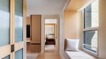 A modern hotel room with a large window, wooden flooring, and a cozy seating area by the window.
