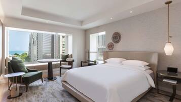 A modern hotel room with a large bed, a seating area with a table, and a view of the cityscape.