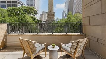 A balcony with two wicker chairs and a small table, overlooking a cityscape with modern buildings and a historic tower.