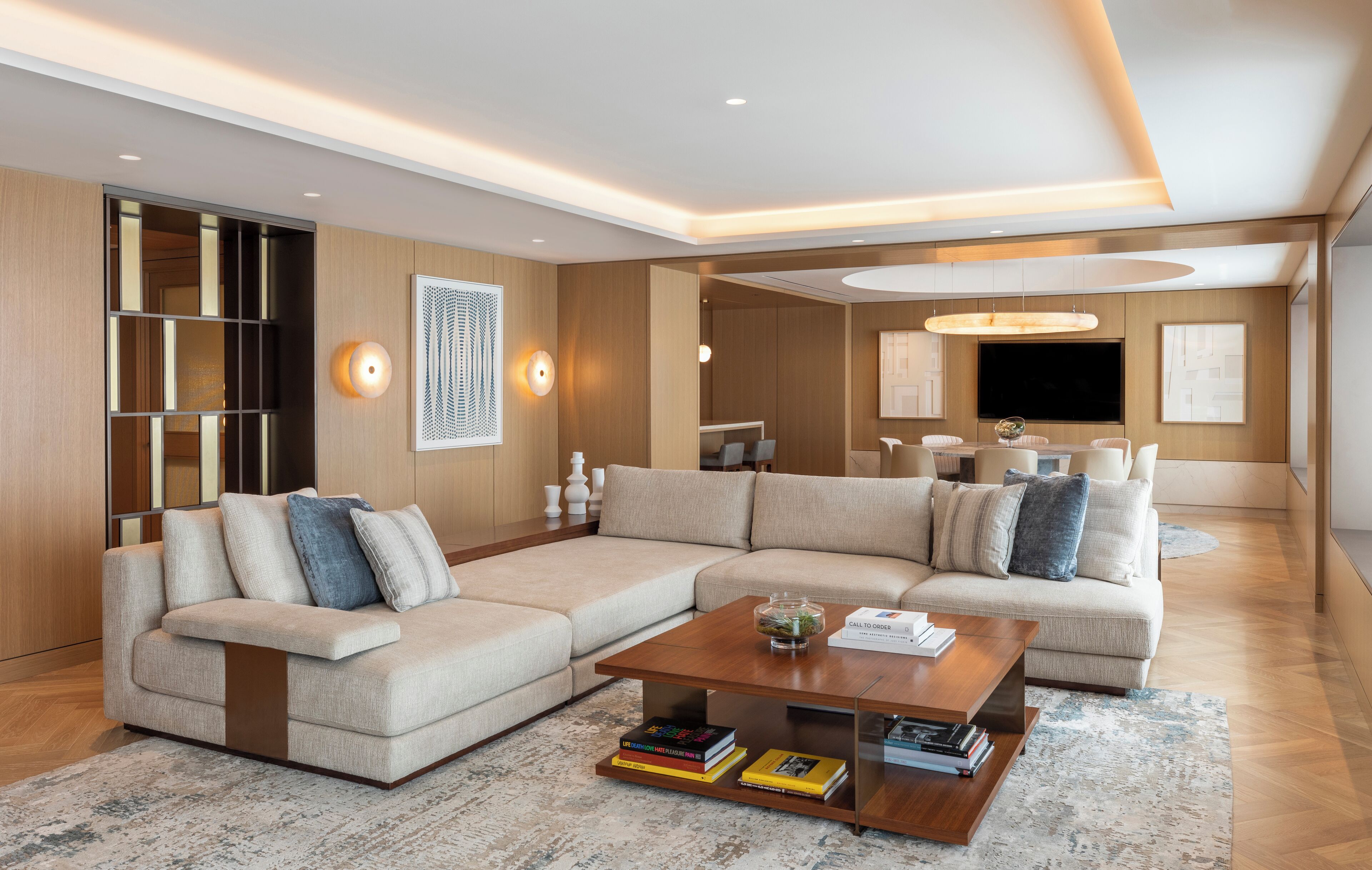 A modern living room with a sectional sofa, a coffee table with books, and a large flat-screen TV.