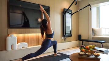 Una esterilla de yoga en el suelo, un televisor montado en la pared, un banco de madera y un frutero sobre una mesa.