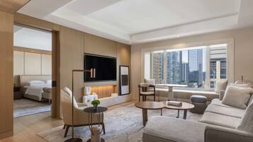 A modern living room with a flat-screen TV, comfortable seating, and a large window offering a city view.
