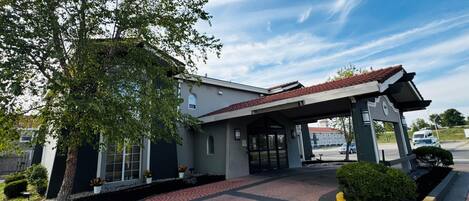 Un edificio con vestíbulo cubierto, un árbol y un camino de entrada pavimentado.