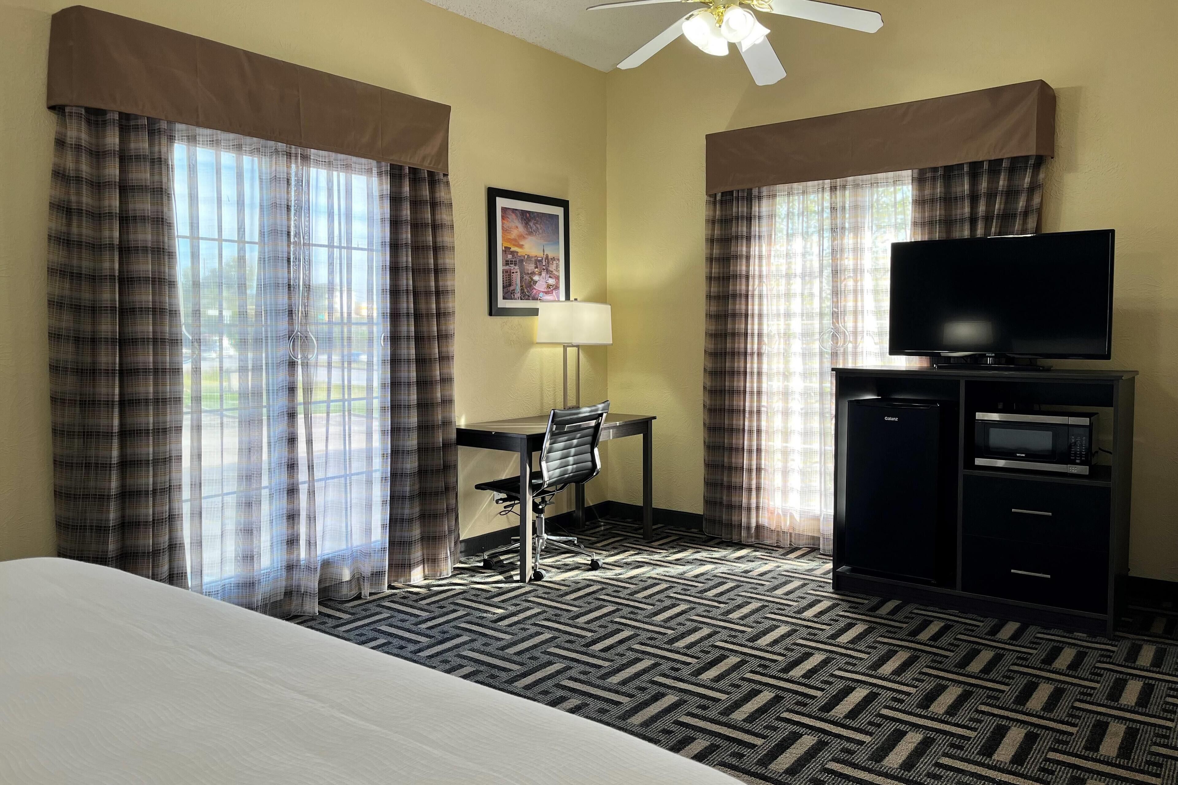 A hotel room with a bed, a desk with a chair, a television, a microwave, and a refrigerator.