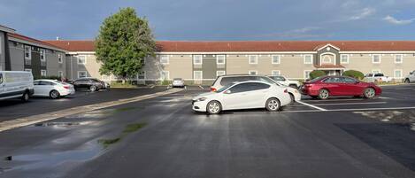 A parking lot with several cars, a building with a red roof, and a tree in the foreground.