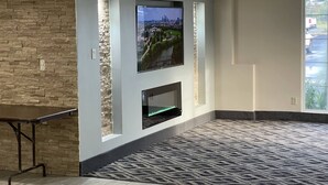 Una sala de estar moderna con una pared de acento de piedra, un televisor montado, una chimenea y una alfombra estampada.