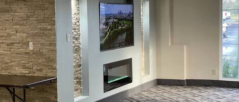 A modern living room with a stone accent wall, a mounted TV, a fireplace, and a patterned carpet.
