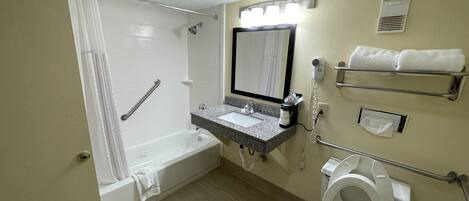 A bathroom with a bathtub, toilet, sink, and a shower with a handrail.