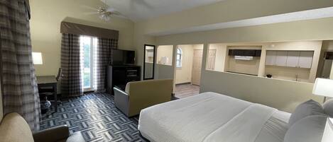 Una habitación de hotel con una cama grande, un escritorio con silla, televisión y ventilador de techo.