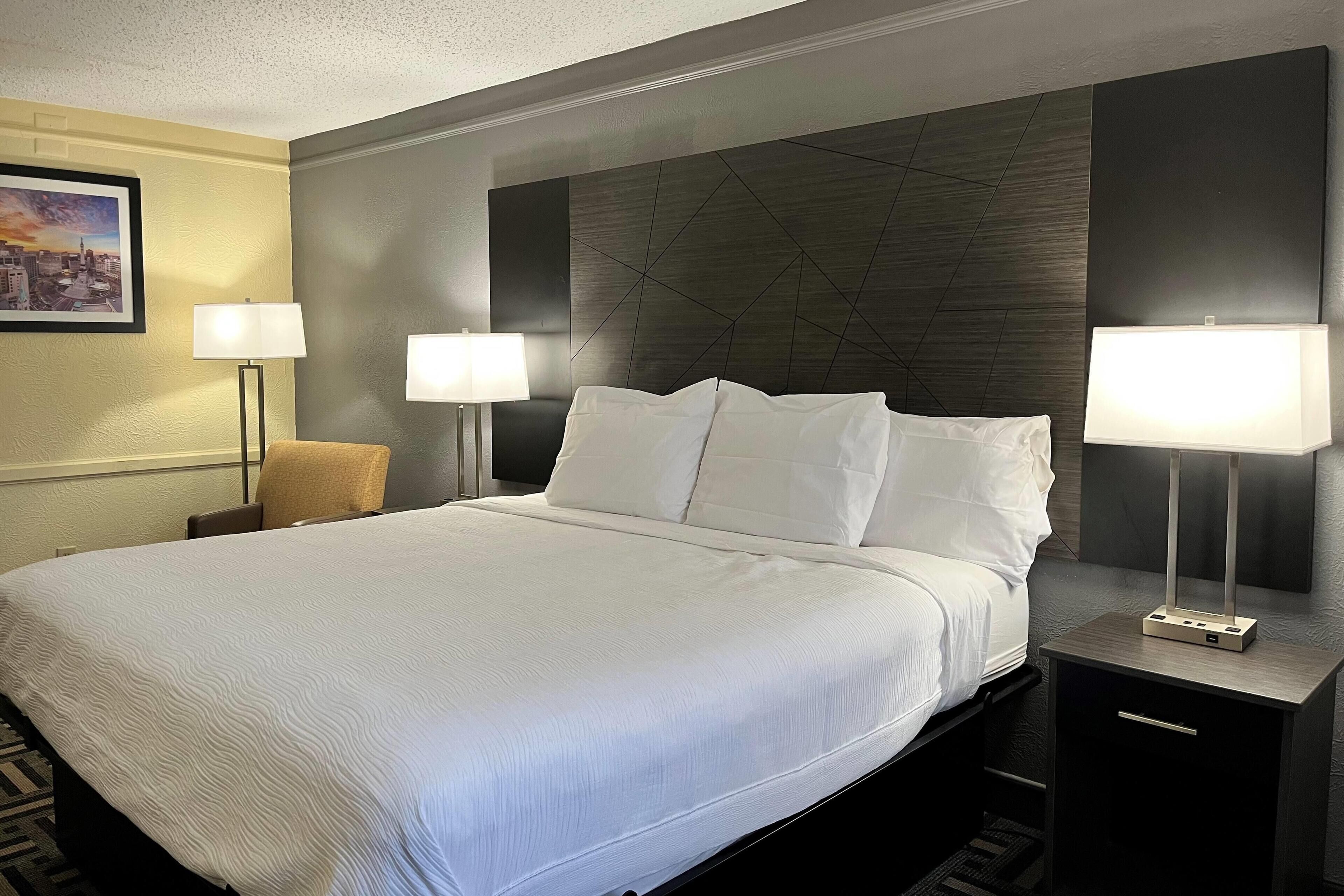 A hotel room with a large bed, two bedside lamps, a nightstand, and a framed picture on the wall.