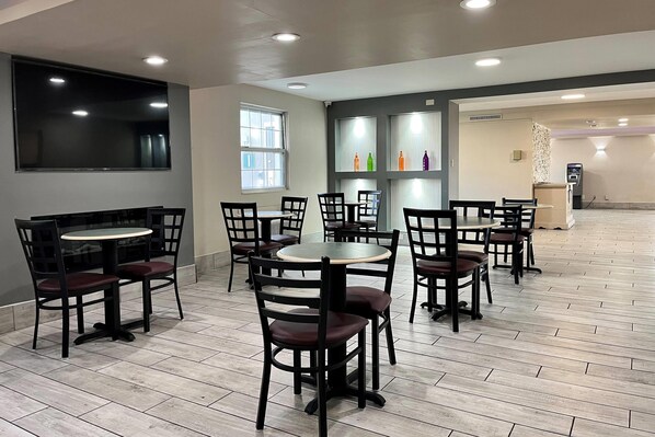 A spacious indoor area with multiple round tables and chairs, a large flat-screen TV mounted on the wall, and a vending machine in the background.
