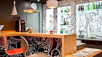 Una zona de bar con mostrador, asientos y una pared con arte abstracto en líneas.