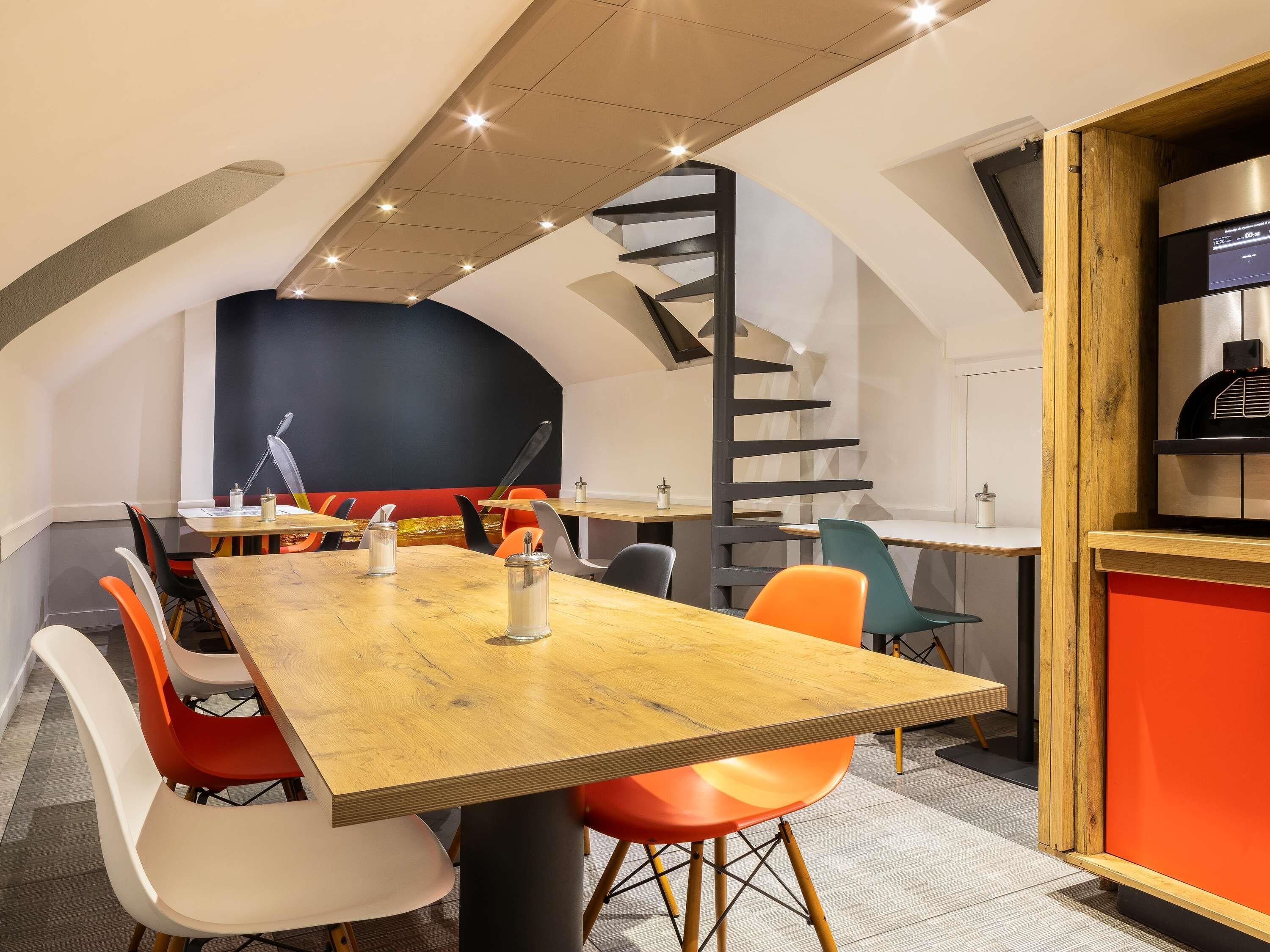 A modern dining area with a wooden table, colorful chairs, and a spiral staircase.