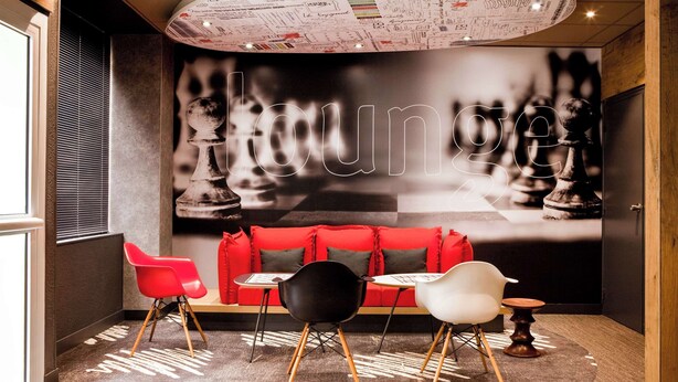 Ein moderner Lounge-Bereich mit einer Wand zum Thema Schach, einem roten Sofa und verschiedenen Sesseln.