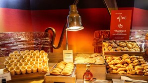Ein Frühstücksbuffet mit verschiedenen Gebäcksorten, einer Ahornsirup-Flasche und einem Schild, das Vitamine bewirbt.