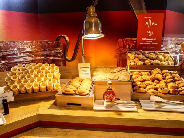 A breakfast buffet with various pastries, a bottle of maple syrup, and a sign promoting vitamins. - ibis Paris Maine Montparnasse 14ème (Paris)